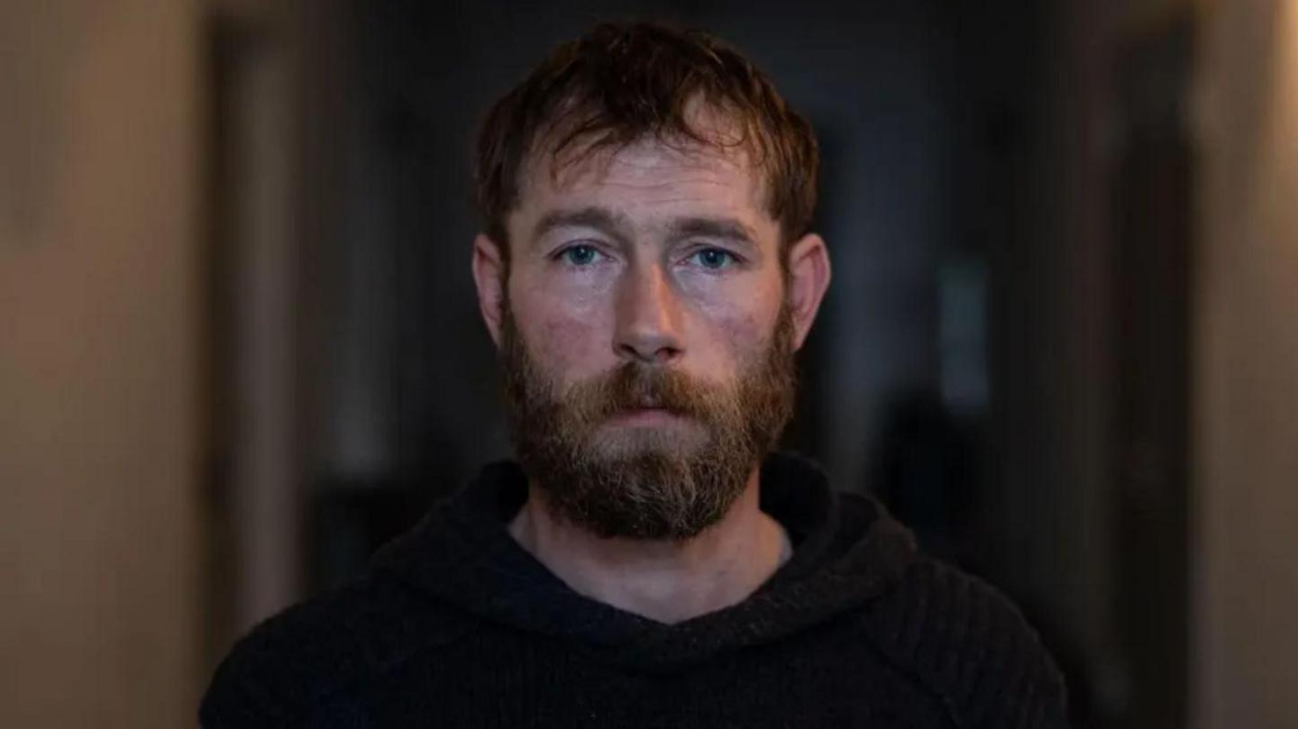 Chris Garrett has brown short hair and a beard. He's wearing a black hoodie.