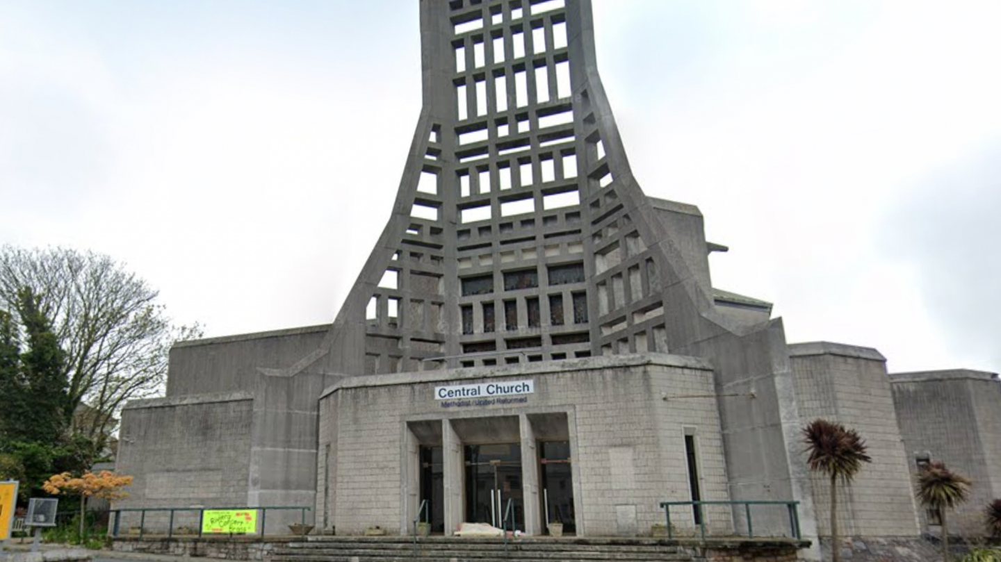 Google street view of Central Church in Torquay. The church is made of grey brick. There are palm trees outside the church. 