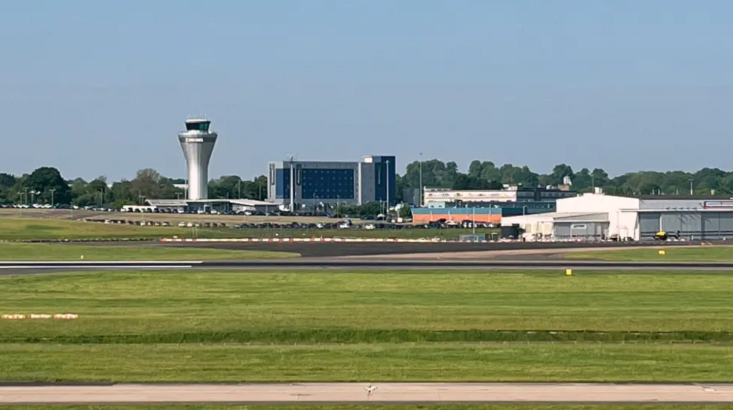 An airport with lots of grass in the foreground and a number of runways and a control tower in the background