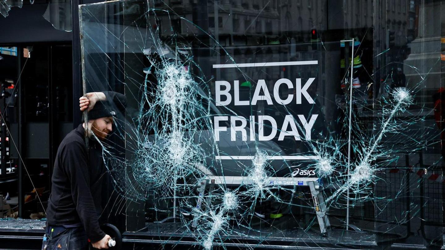 A man works to remove a broken window from a sport shop that was damaged in a riot