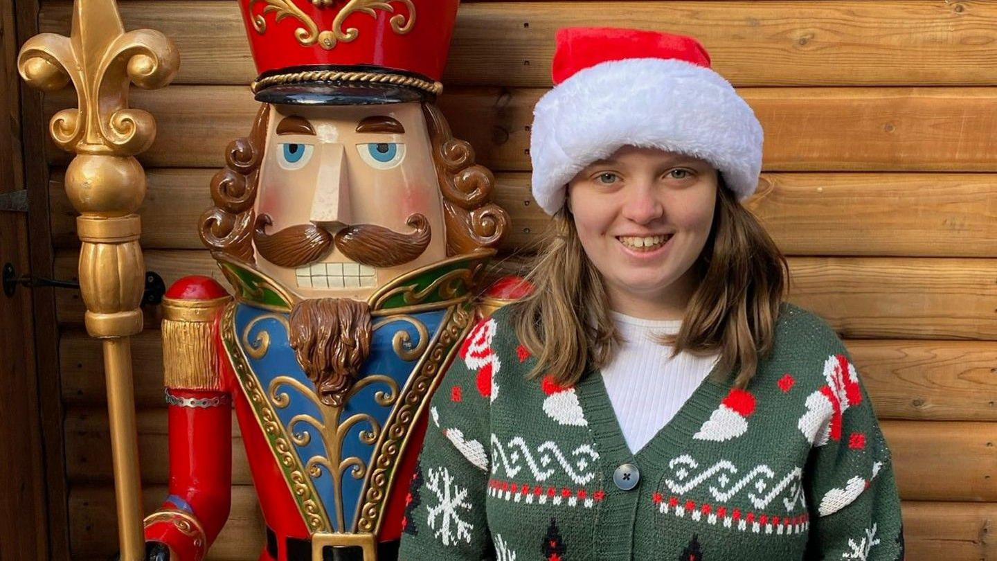 Hannah yn gwenu mewn siwmper Nadolig a het Sion Corn