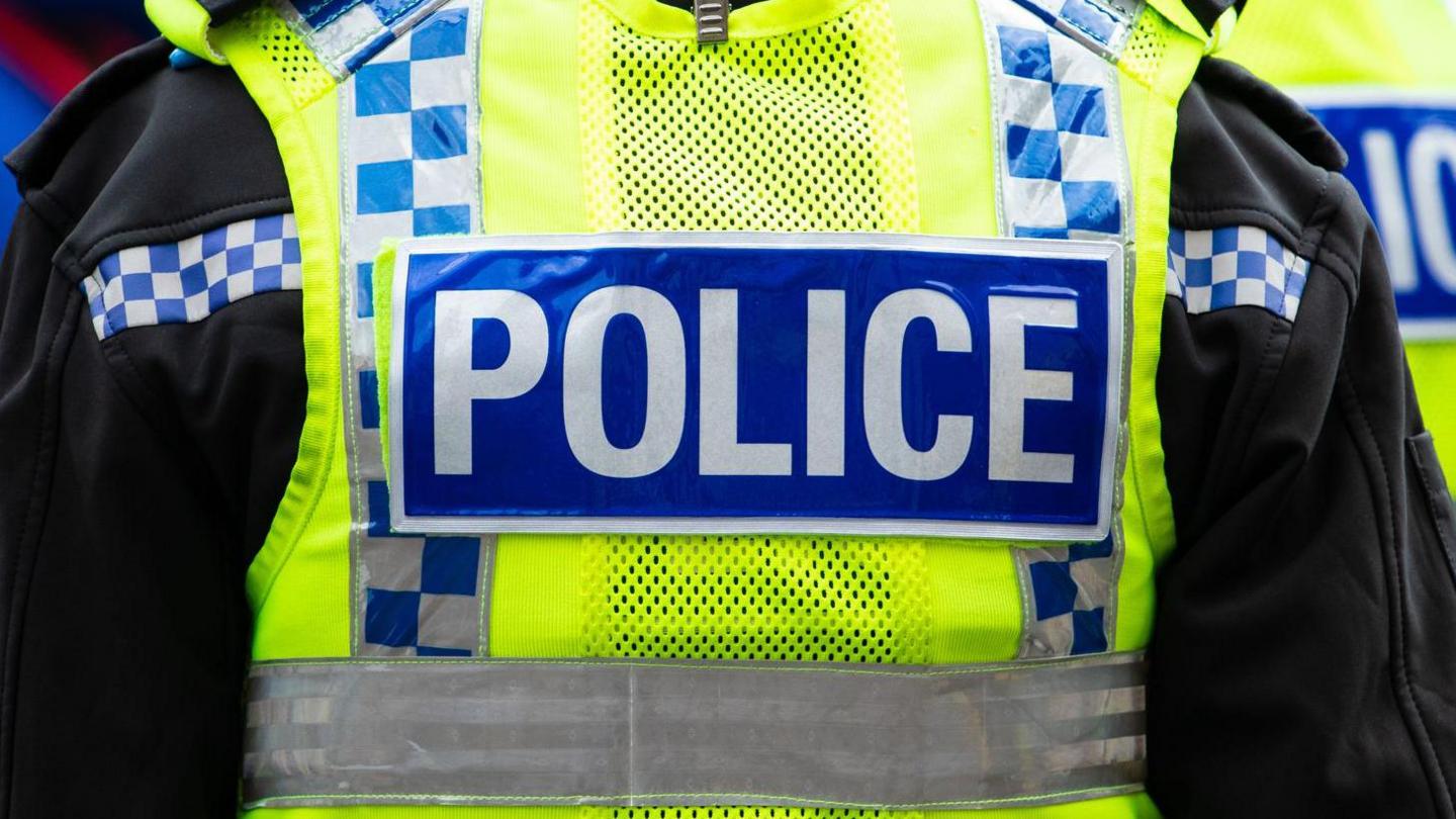 The back of a police officer's yellow high vis vest. It says "Police" in white on a blue strip.
