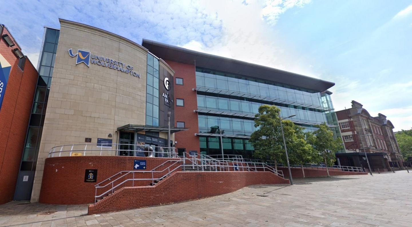 General view of the University of Wolverhampton. The sign of the university is visible against a blue sky with clouds and there are paving stones in front of the building. 