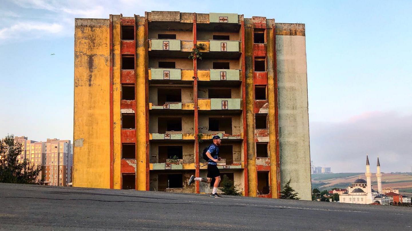 A man runs down a hill in front of a derelict building.