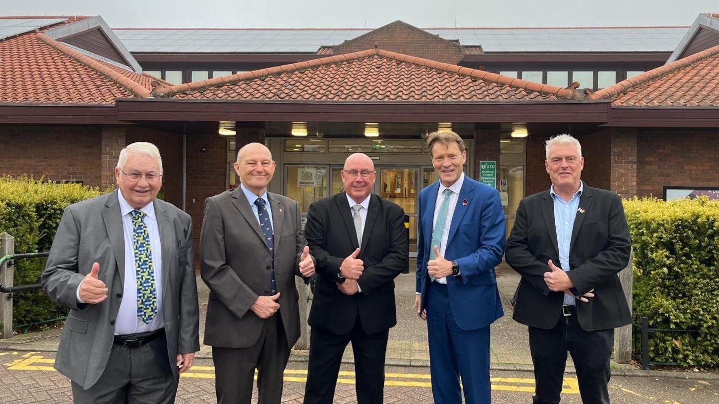 Five men in suits smiling and giving a thimbs up sign outside of the council offices. The three councillors are the first three from left, and are pictured with Reform top brass Richard Tice and Lee Anderson