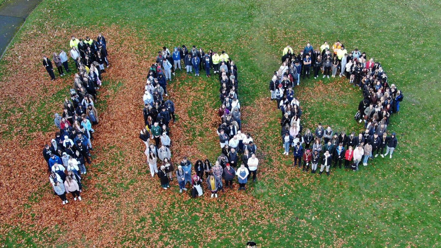A group of people stood in a field, making the shape of the numbers 100