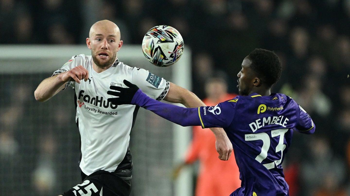 Matthew Clarke of Derby County battles for the ball with Siriki Dembele of Oxford United