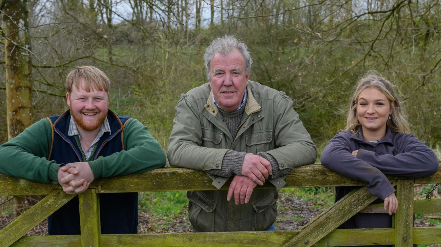 Kaleb Cooper, Jeremy Clarkson and Harriet Cowan leaning on a fence