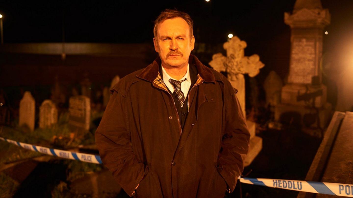 A man stands in front of a police tape at an industrial location.