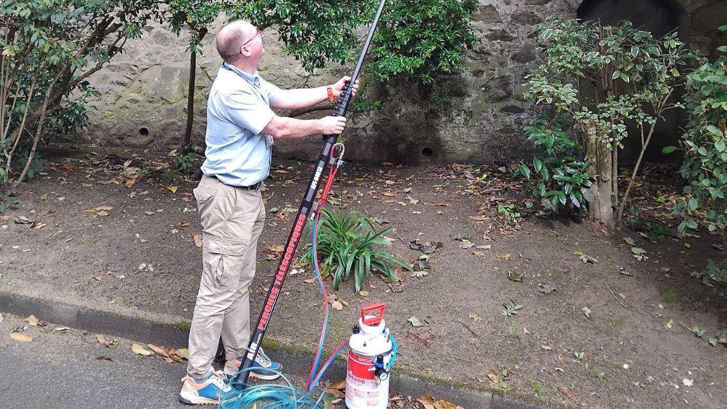 The image shows a partially bald man wearing glasses, a blue short-sleeved top, beige cargo trousers and blue trainers holding the new lance which is black with white and red writing along it. A white pump can also be seen positioned next to him with a light blue tube connecting it to the lance. 