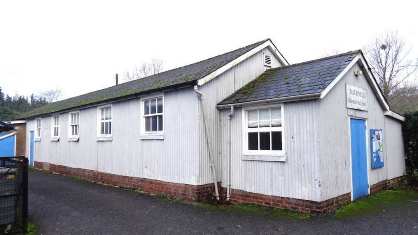 A white-walled wooden building with a grey tiled roof and a blue door