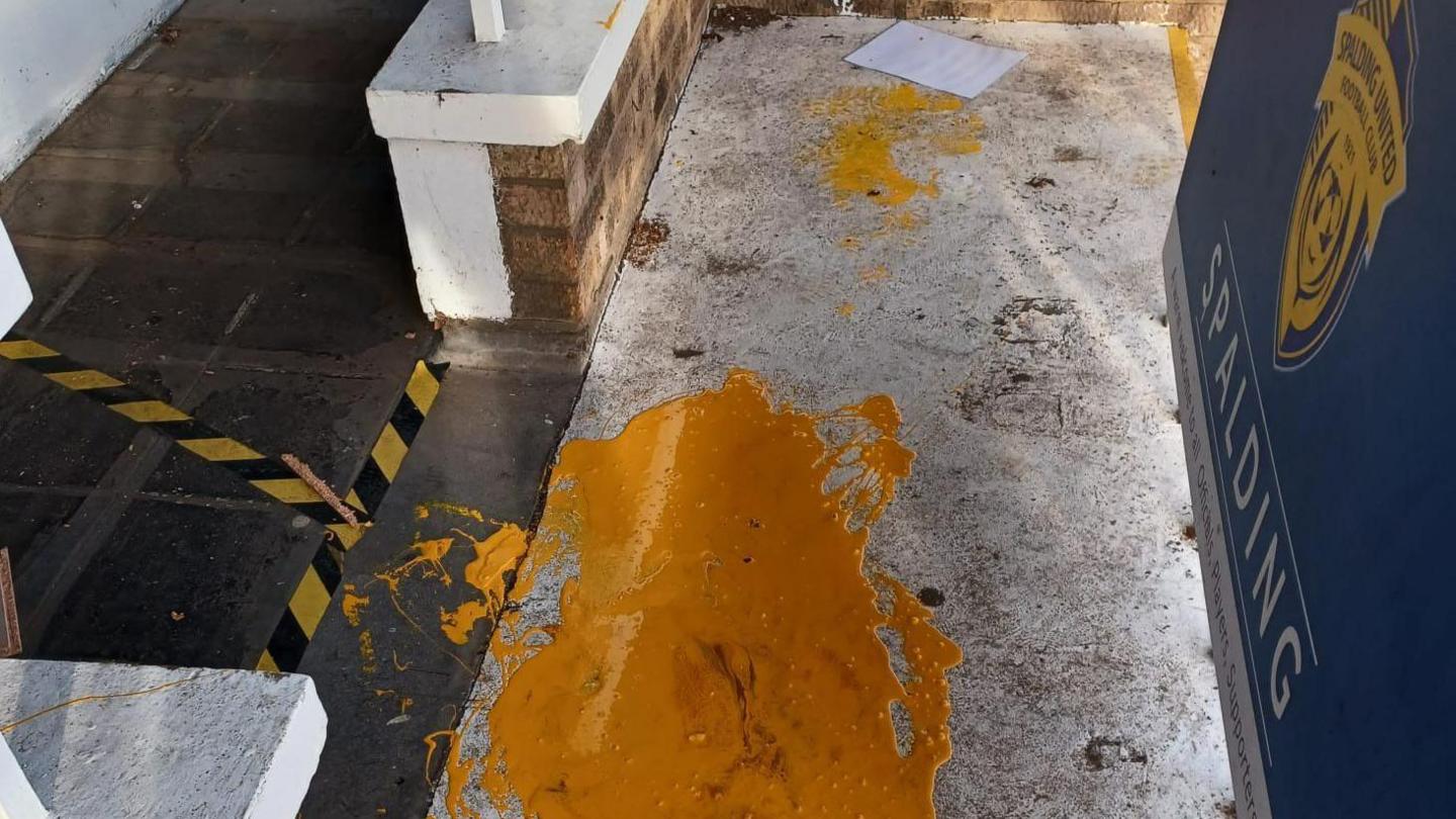 Orange paint is spilt on a floor next to a blue Spalding United FC poster