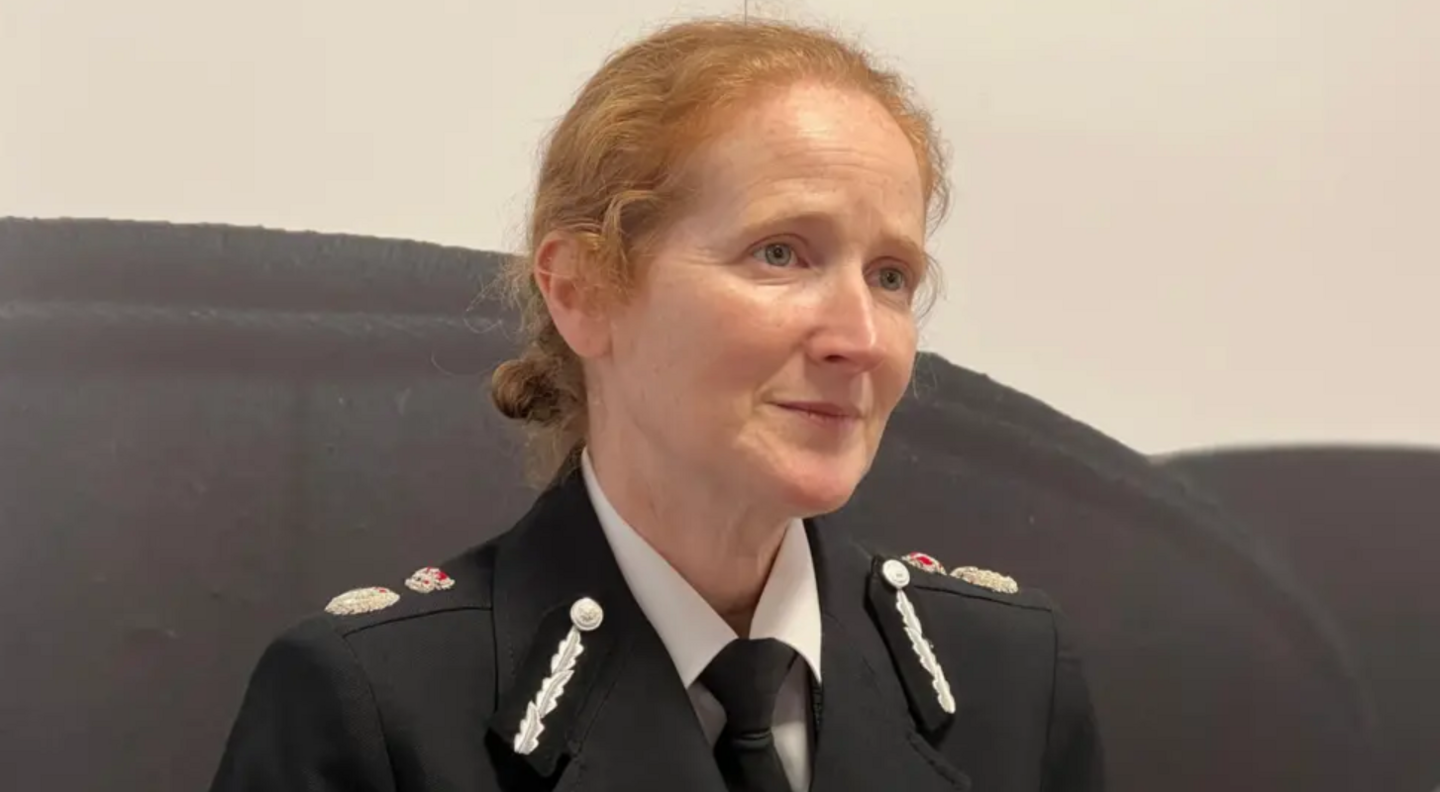Catherine Roper wearing a black and white police uniform which includes a black tie, white shirt and silver brooches. She has orange hair and is looking off camera.