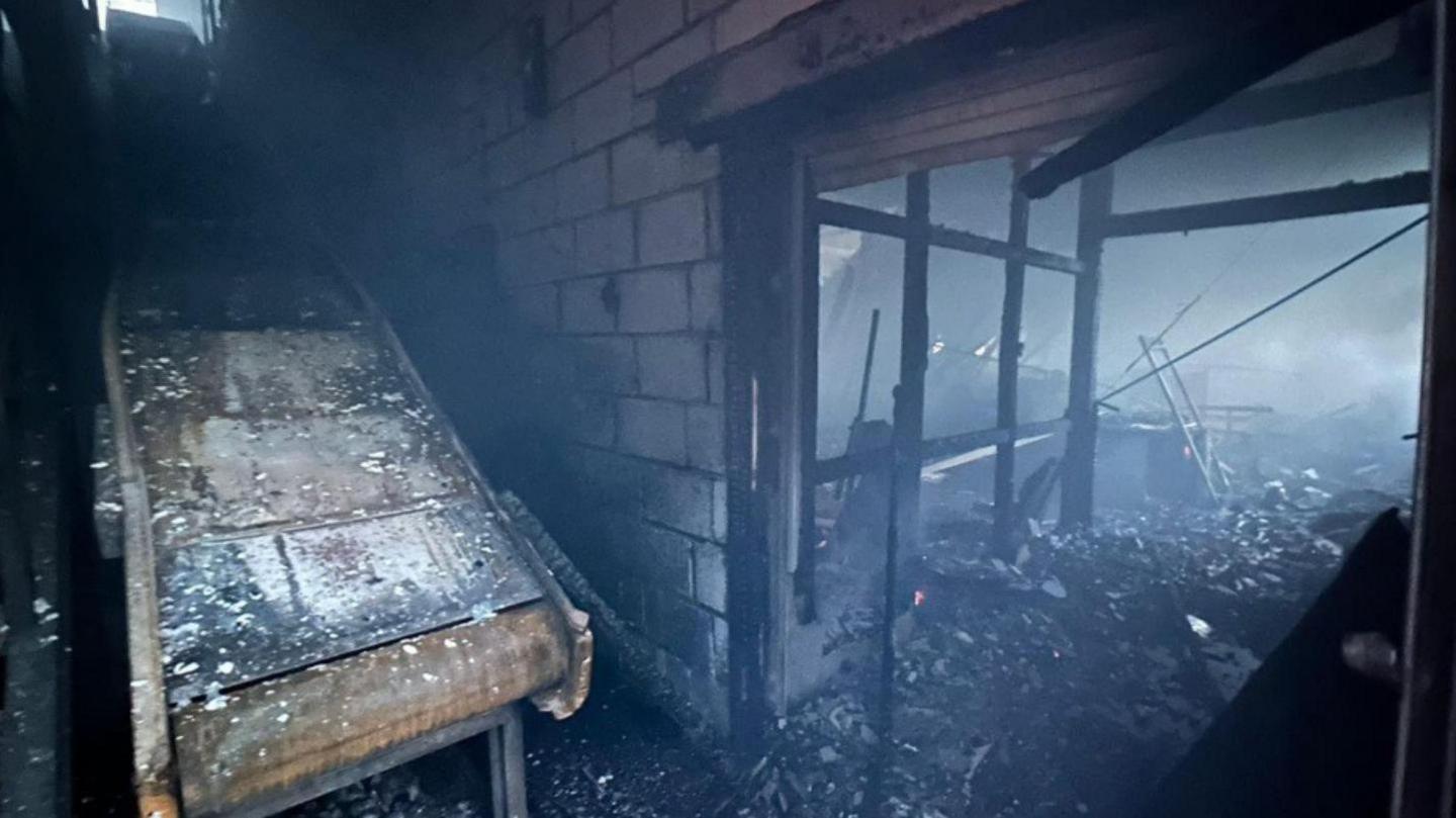 The burnt out interior of a derelict mill on Andrew Street. A door frame is open and the floor is covered in ash. 