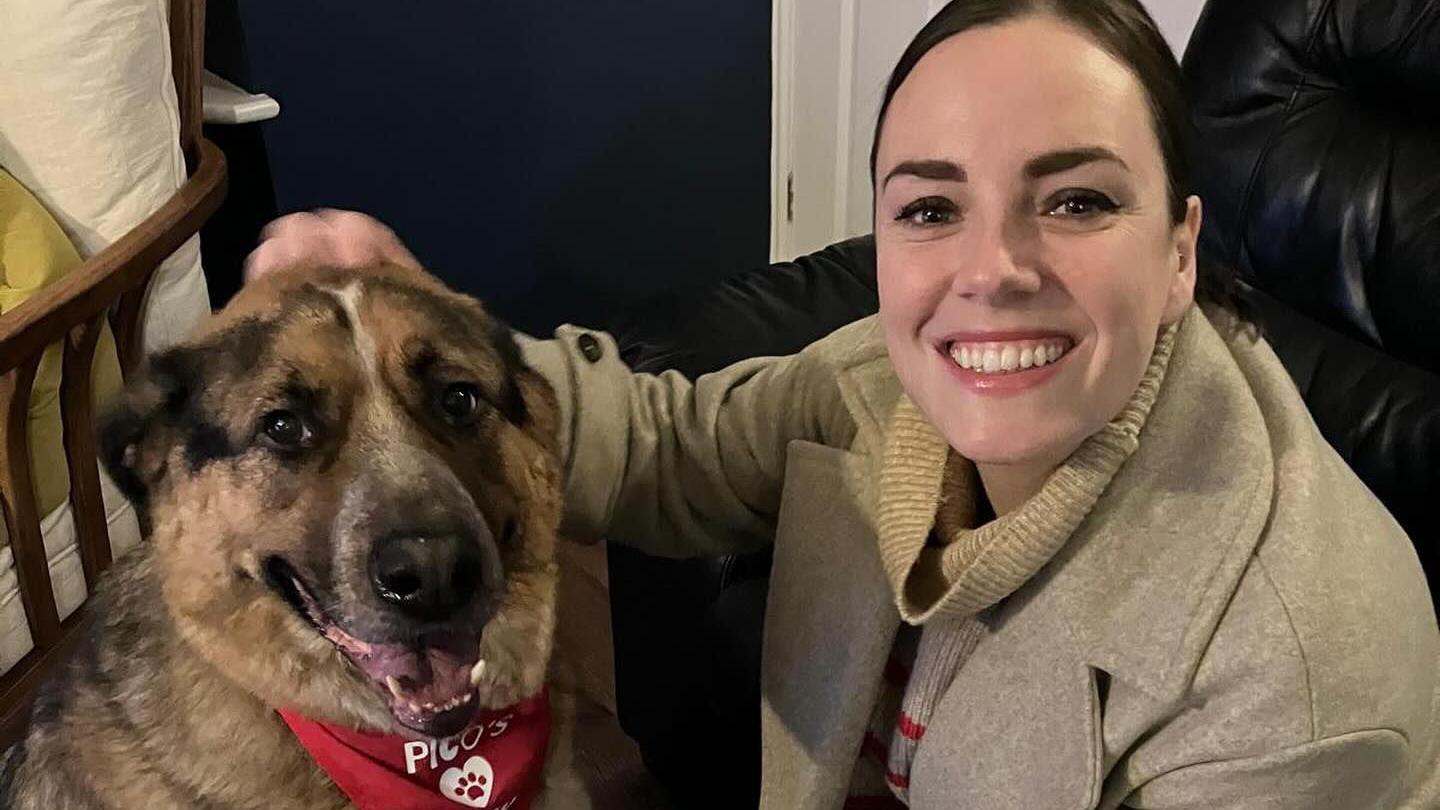 Marissa Keltie pats the head of a dog, while both look into the camera. Marissa is grinning.