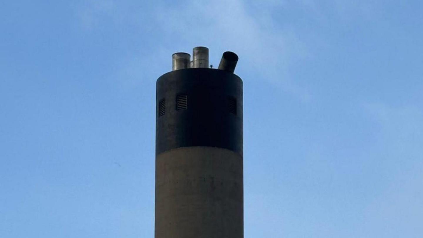 The top of the stack, one of the flue caps has fallen over, on a clear day.