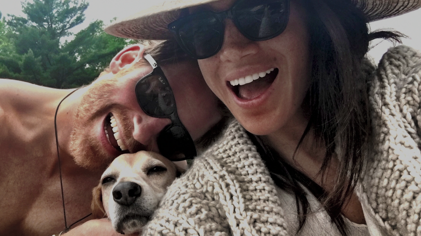 A handout photo shows the Duke and Duchess of Sussex with their late dog, Guy. The two are seen leaning together as the dog pokes his head between their shoulders and looks towards the camera. 