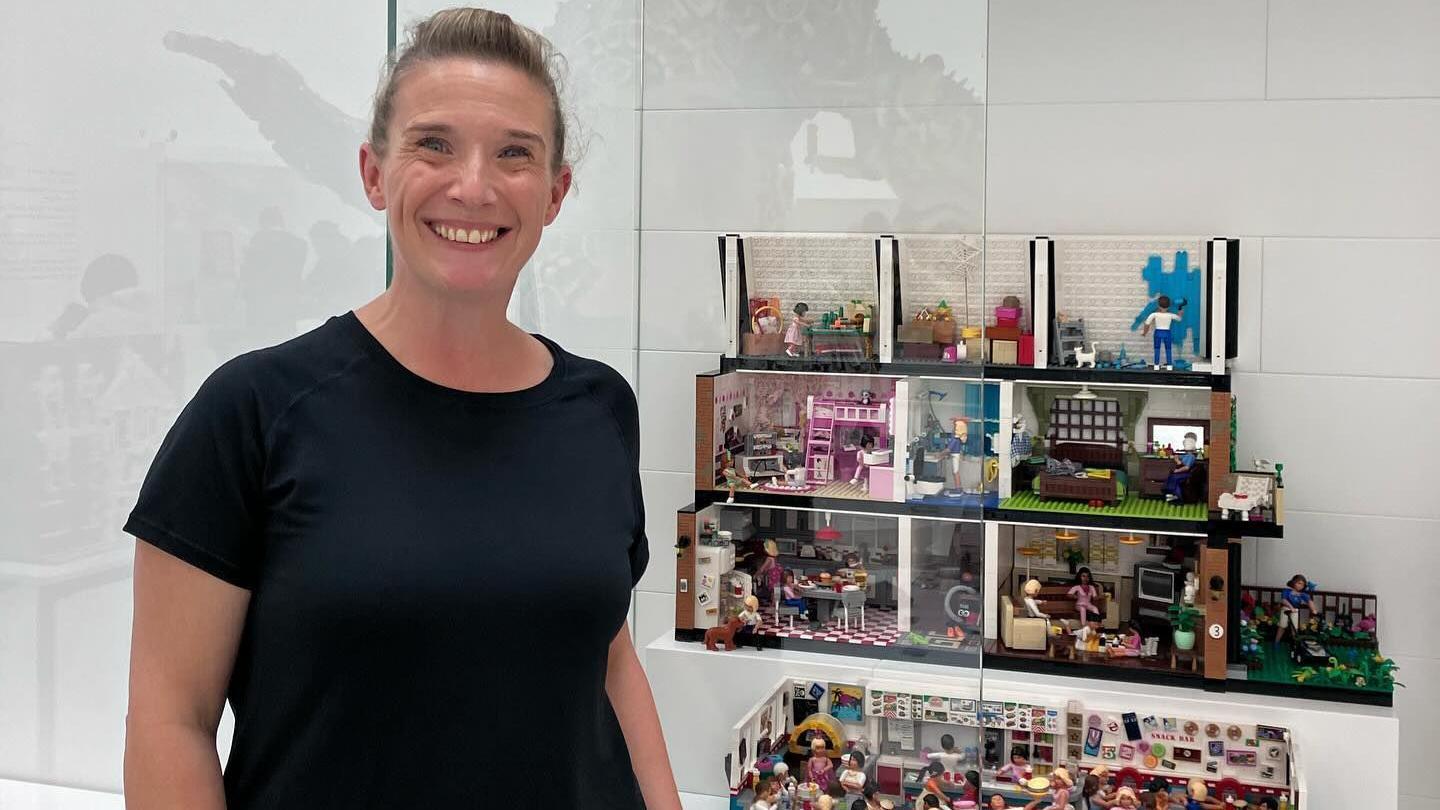 Victoria Worsley is wearing a black t-shirt and is stood in front of a Lego doll's house display at Masterpiece Gallery at Lego House in Denmark