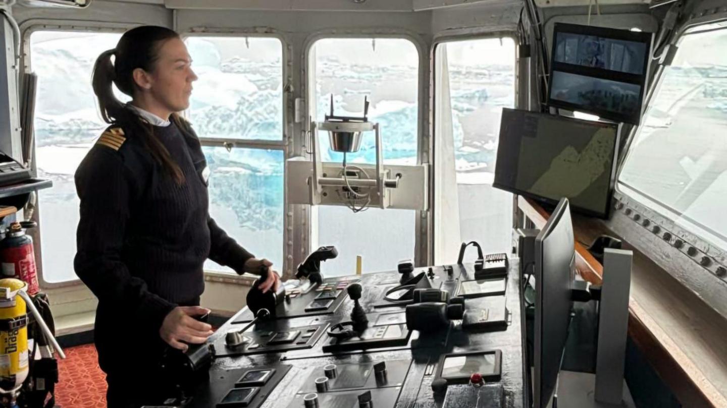 Capt Philippa Bowden in uniform on the deck of a ship in front of lots of controls.