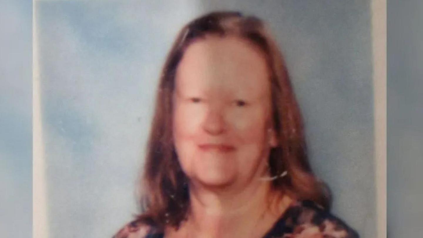 A family photograph of Mrs Johnson who has shoulder-length brown hair. She is smiling at the camera and appears to be wearing a floral top.