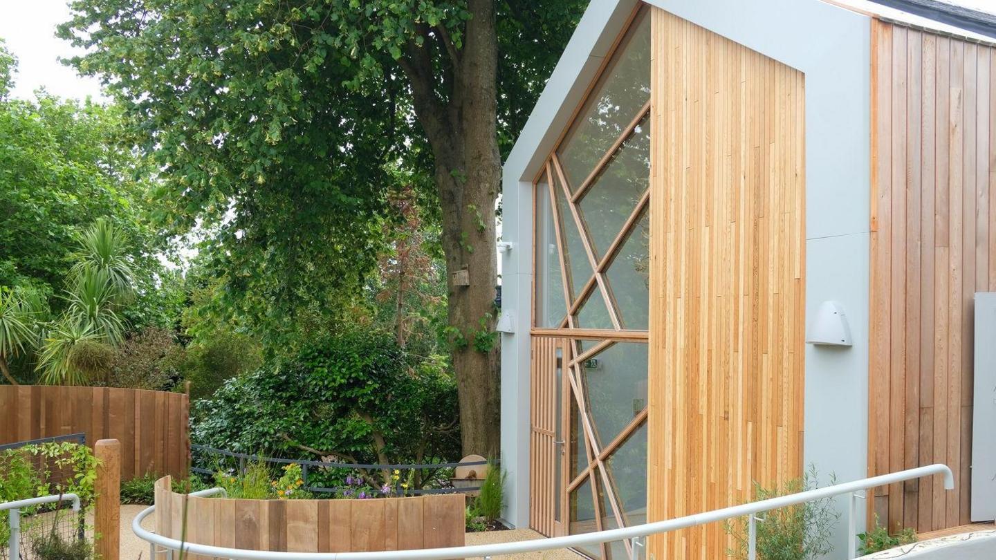 The end of the traditional granite building has a modern extension with large windows and wooden cladding