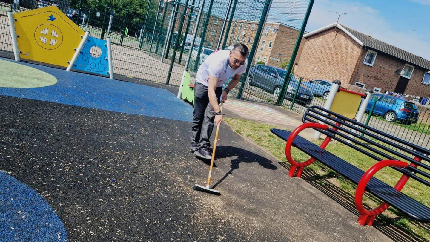 Romeo Mustata with a broom, sweep the ground inside a children's play area.