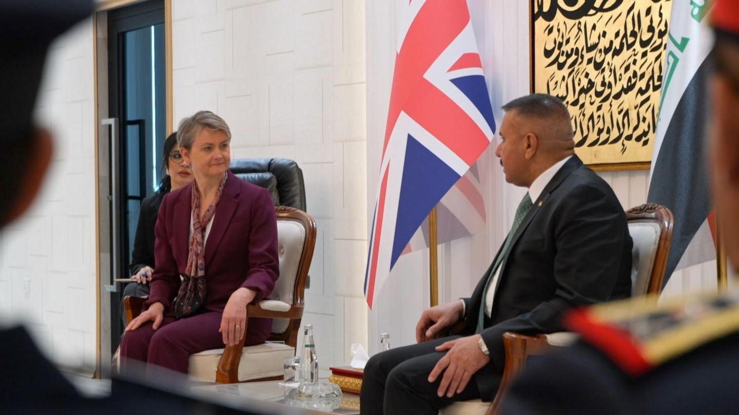 Yvette Cooper and Abdul Amir Al Shammari sitting in chairs side-by-side in front of the UK and Iraqi flags. 