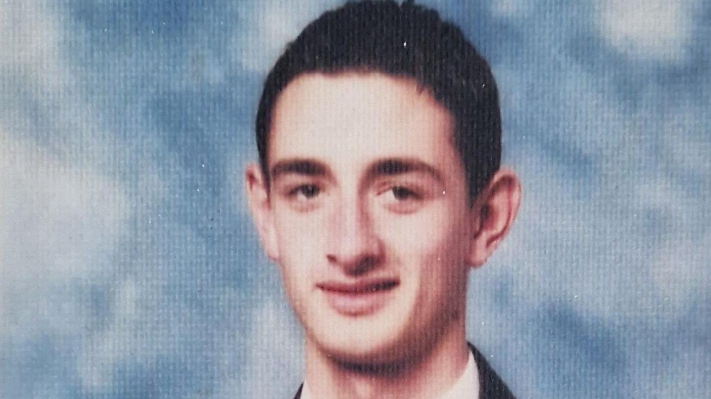 School photo of Gavin Brett looking into the camera with slight smile against a blue and white background