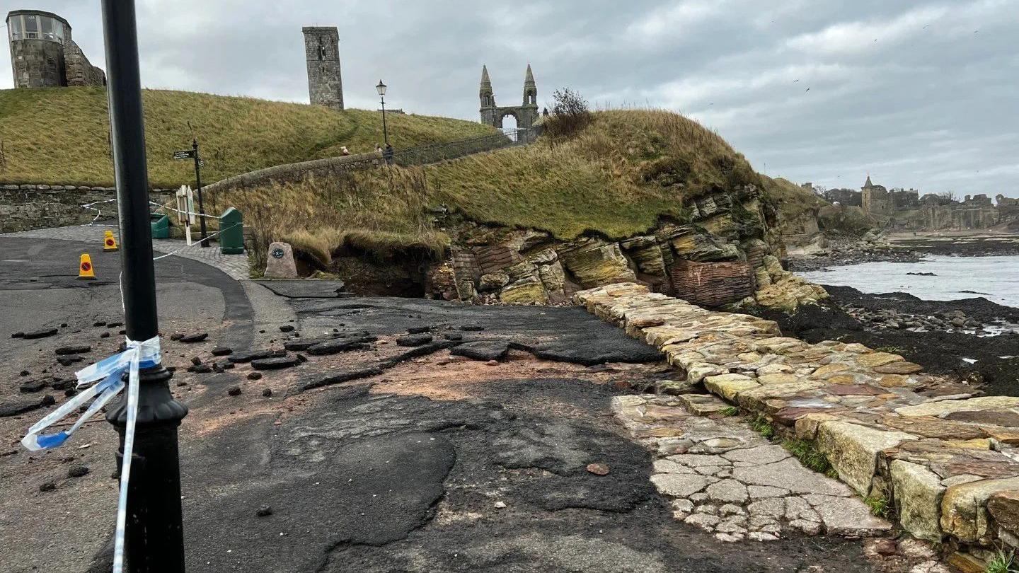 Damages road beside the cobbled pier with hills and spires in the background