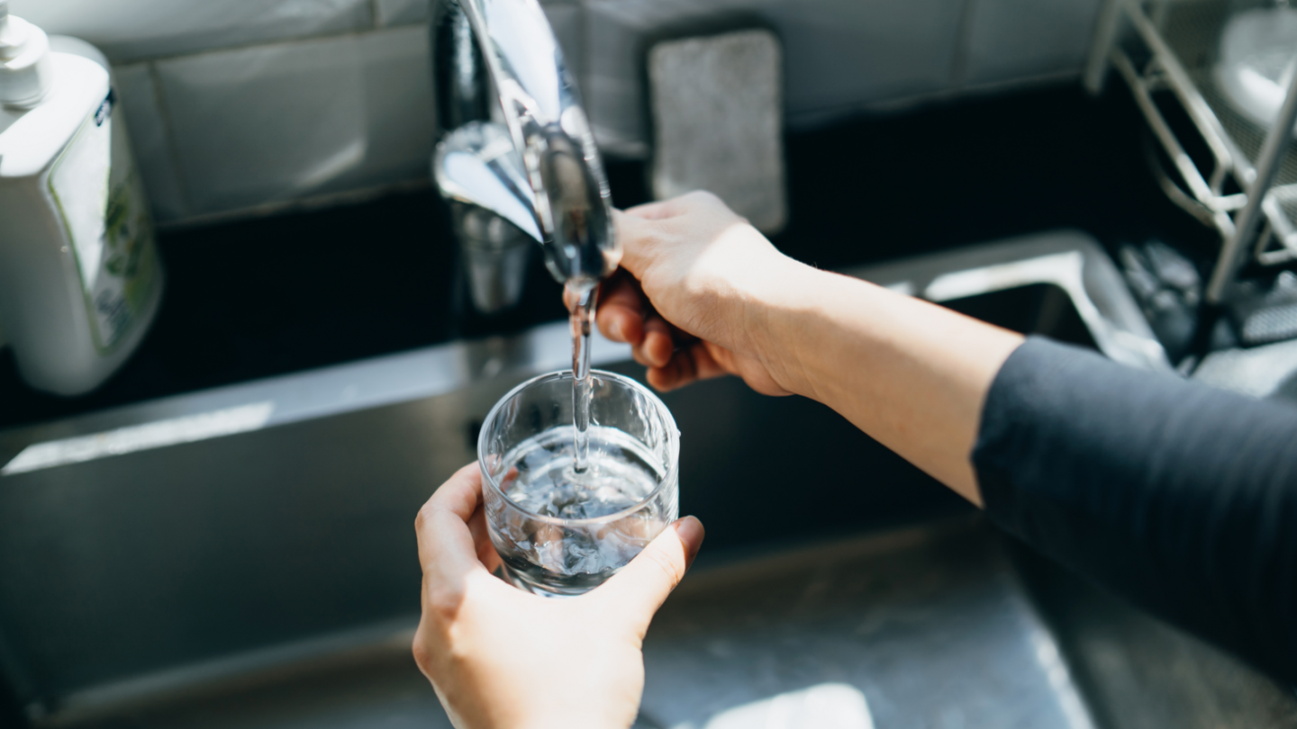 A person filling a glass with water from a kitchen tap.