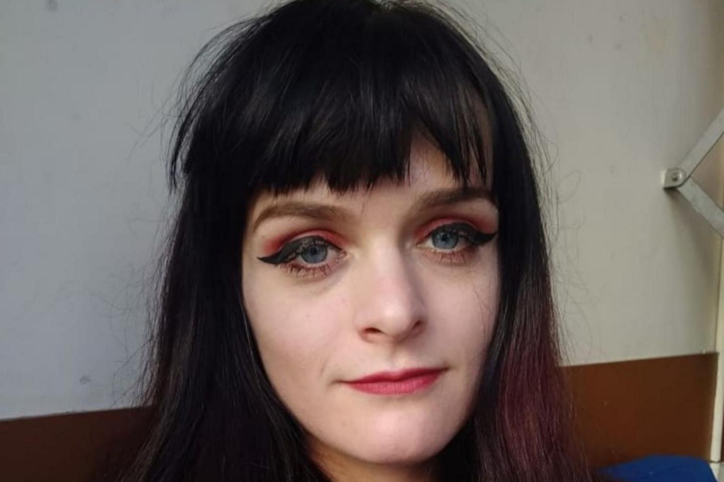 A selfie of a woman who has long, dark hair including a fringe. She is sitting on a sofa and is wearing a dark navy blue jumper.