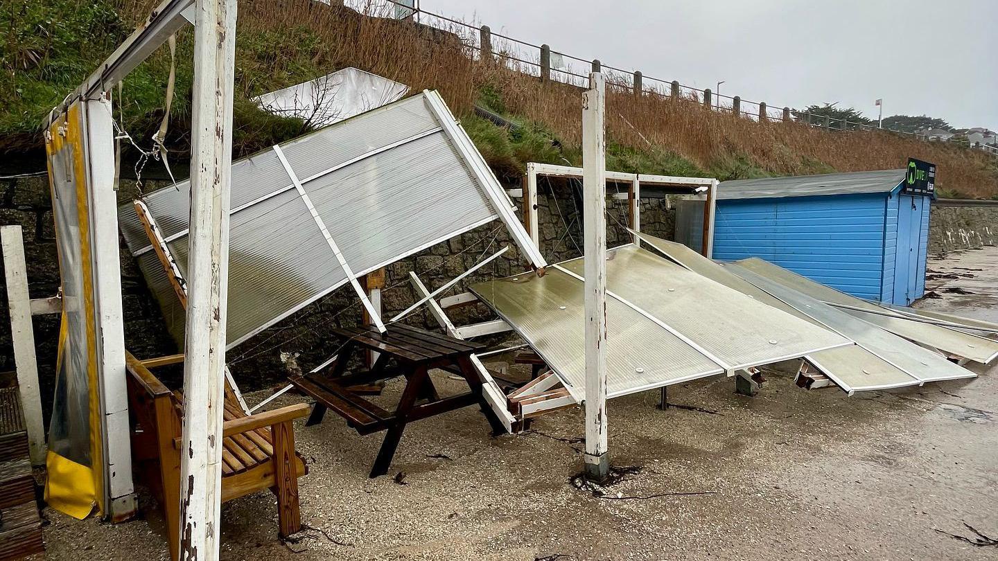 Screens and other beach shelter paraphernalia blown over, with a blue beach hut to the right.