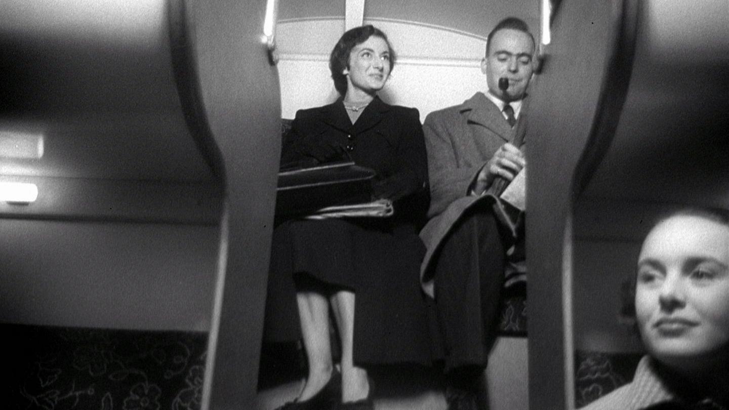 A man and woman sitting on the top deck of a double-decker train