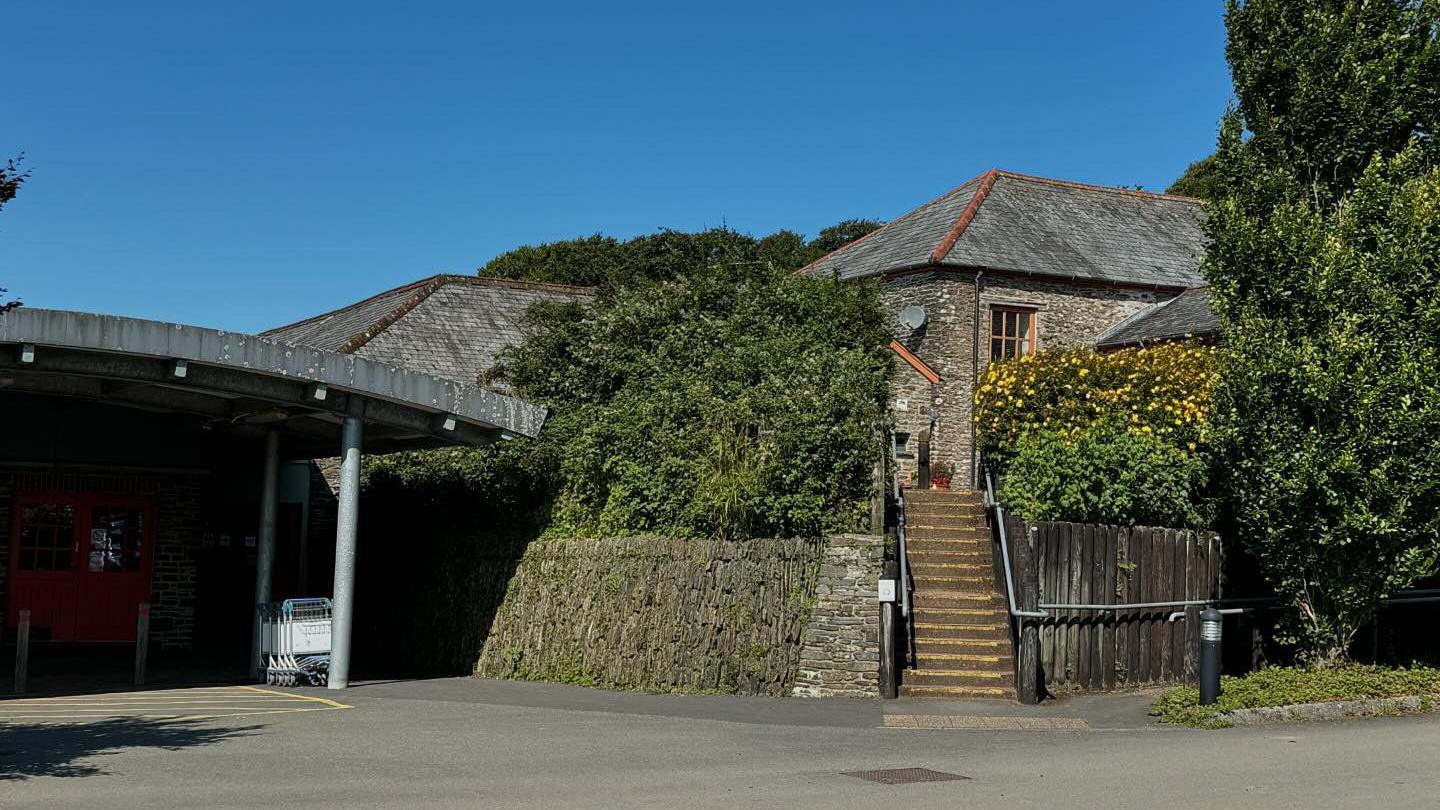 A building made of brick surrounded by trees and plants with a blue sky in the background. 