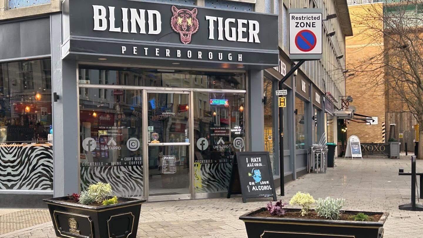 Exterior of the Blind Tiger venue- with a black signboard and a red Tiger emblem on it, with black plant pots placed on the ground outside the bar.