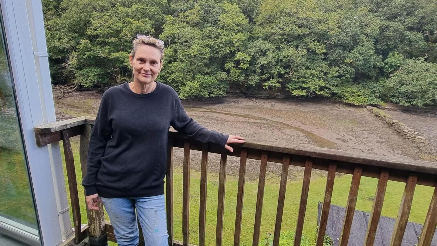 Woman stood on a balcony with a creek and woods behind