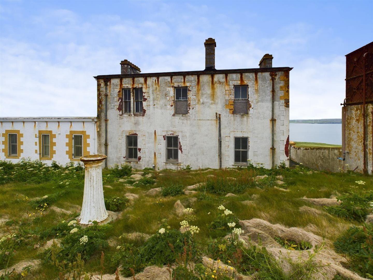 A run down white two-storey building with a grass courtyard and bird bath in the centre