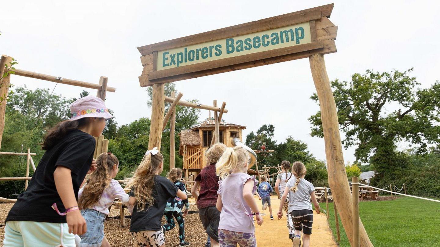 A group of children run under the welcome sign to the Explorers Basecamp play area at the Bristol Zoo Project