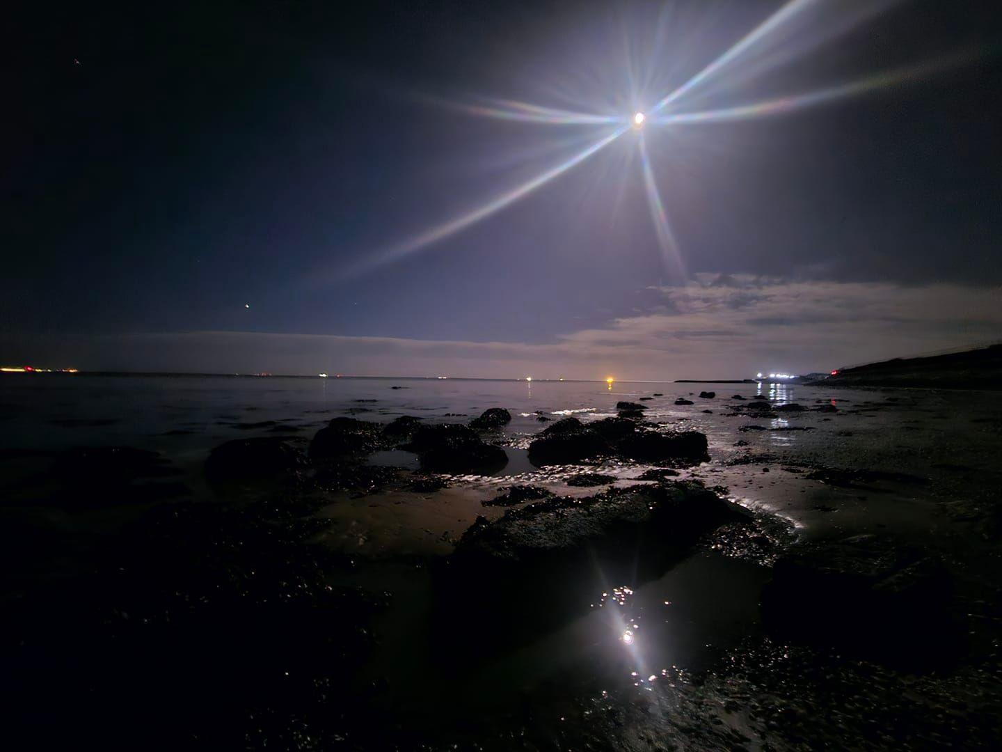 A photo of the full moon above the beach at low tide.