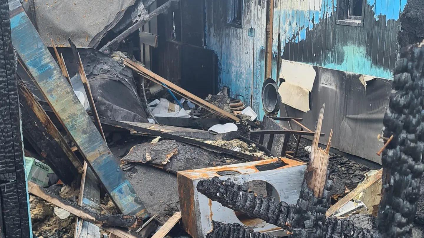 A burnt out shell of a business, showing charred wood, smoke damaged items, and ash. 