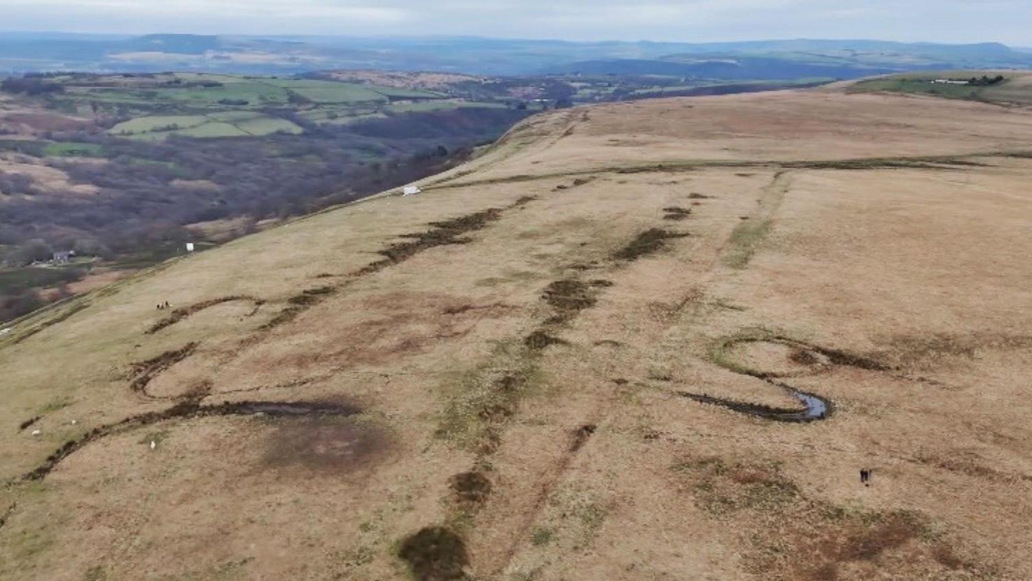 Carnedd Tor Clawdd o'r awyr - mae modd gweld y tirlun ehangach gan gynnwys cwm a bryniau ar y gorwel.