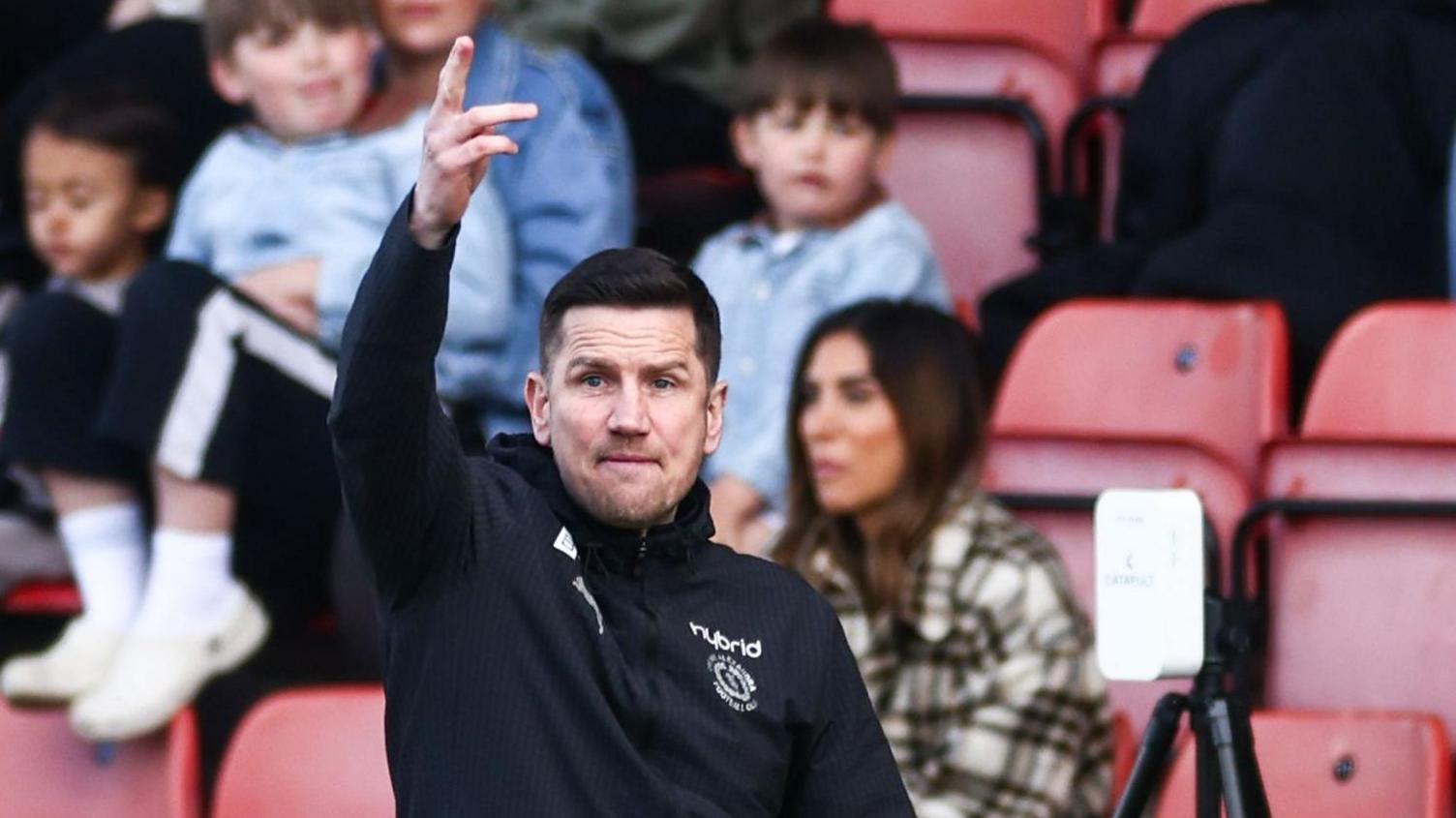 Crewe boss Lee Bell holds his right arm up and shouts instructions from the sidelines during a match.