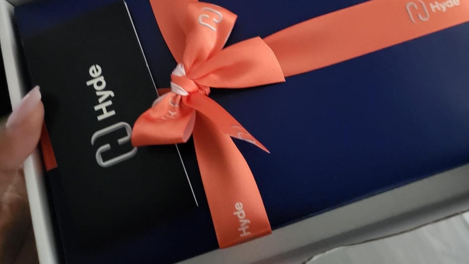 Image of a Hyde-branded blue box of chocolates with an orange ribbon around it, in a box held by Charlene