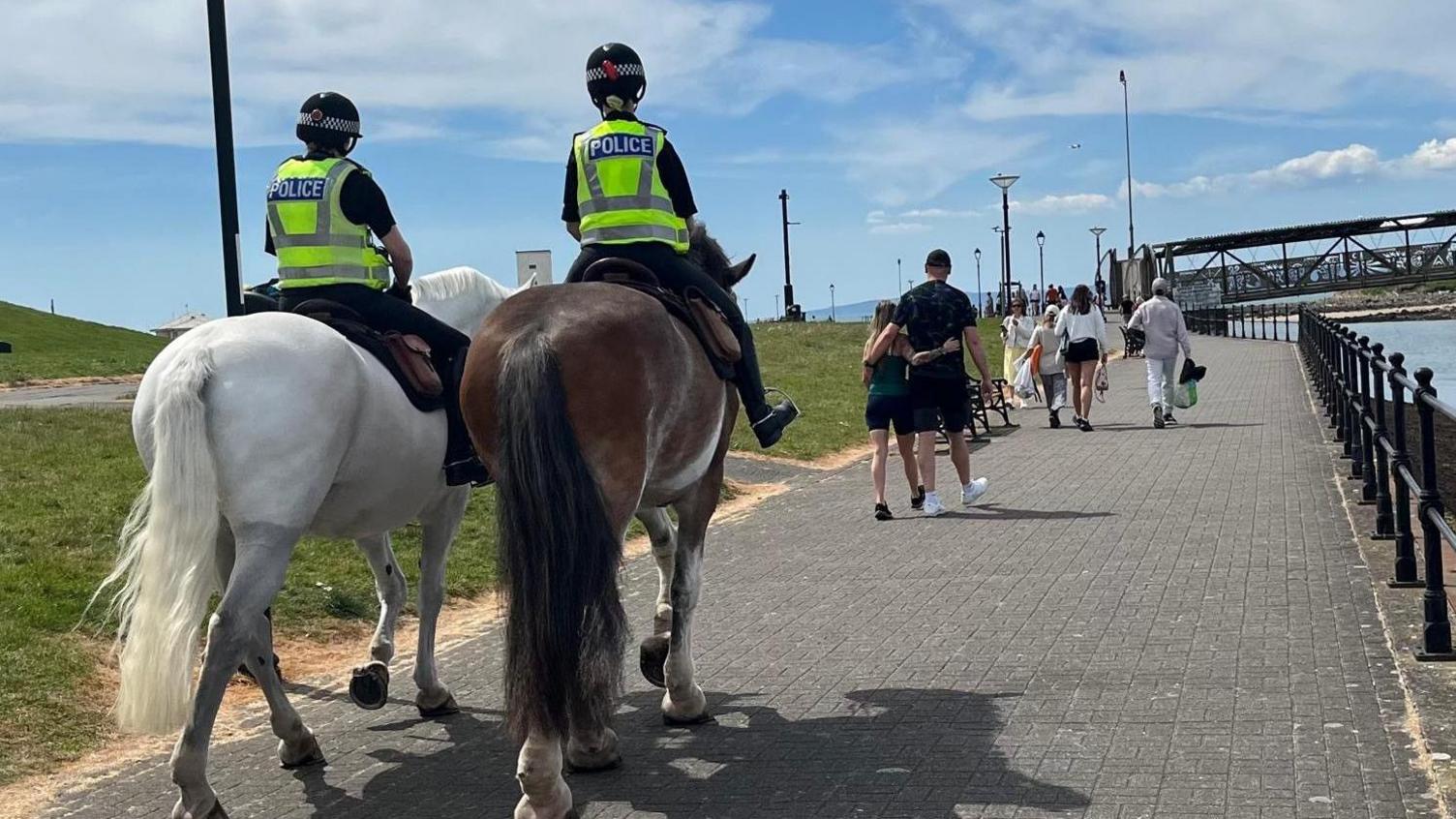 Two police horses patrolling on a path next to Irvine Beach