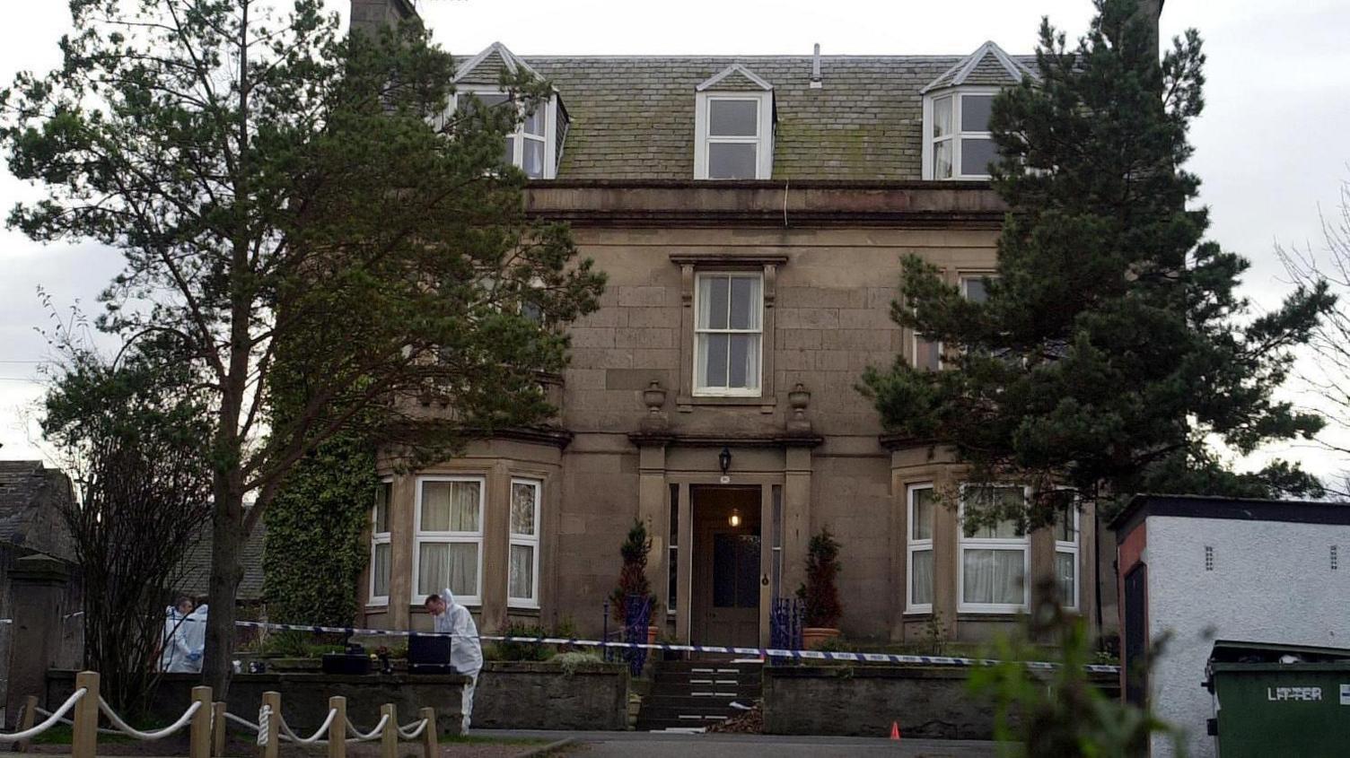 Exterior of the Wilson family home, scene of the murder, with forensic officers wearing white and police caution tape around the property