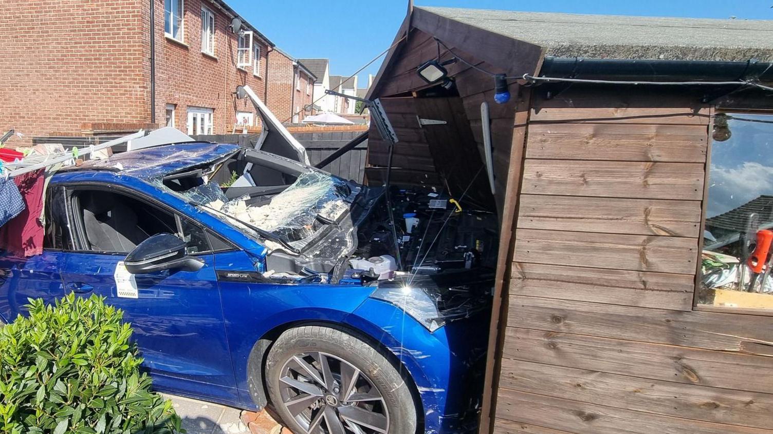 A wide shot of the Blue Skoda crashed into the garden shed.