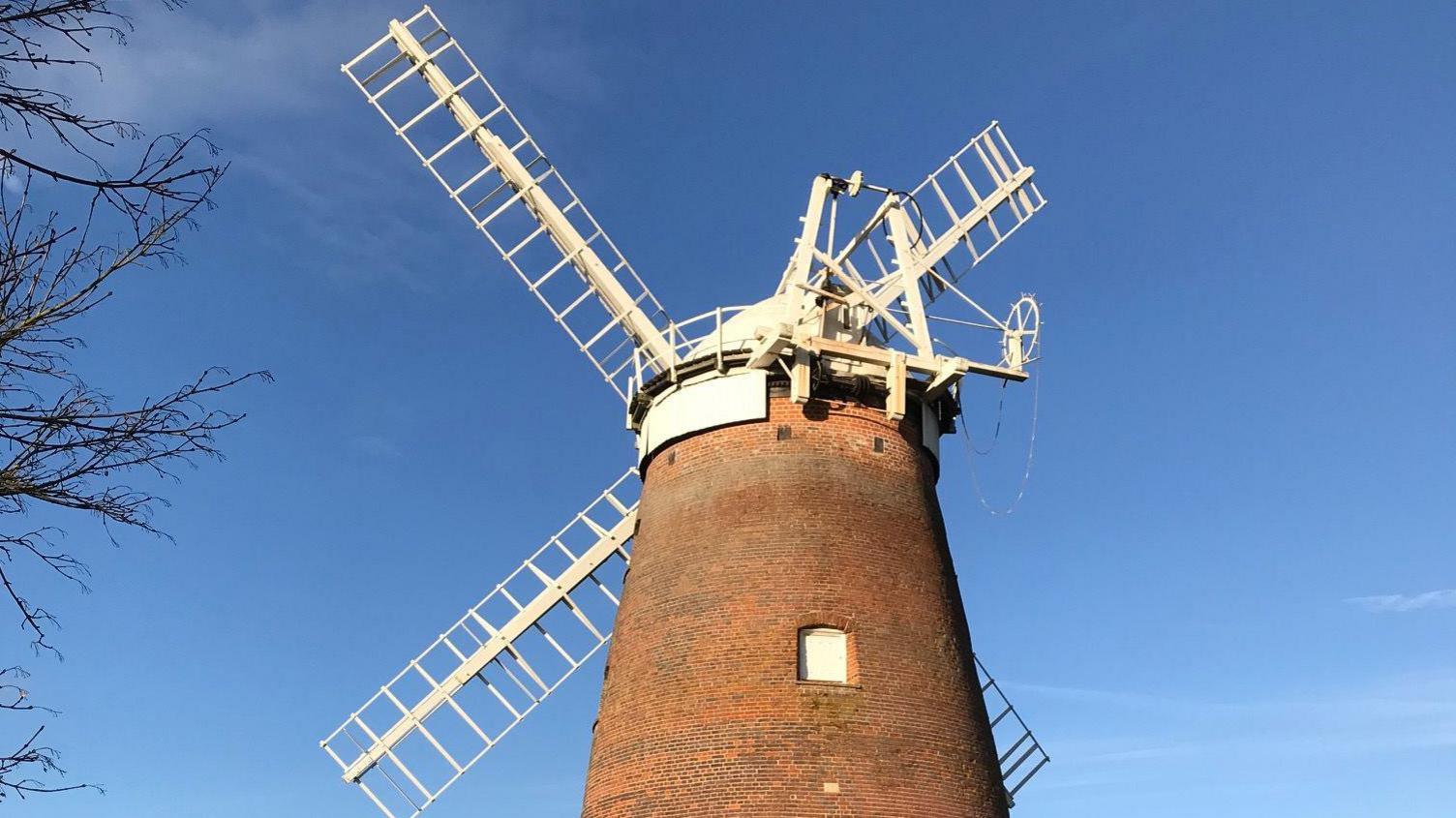 A brick windmill with four white sails pictured on a sunny day