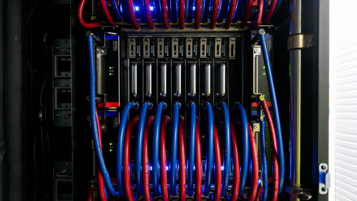 Part of Isambard-AI, showing a black unit with lots of blue and red wires leading in and out of it. 