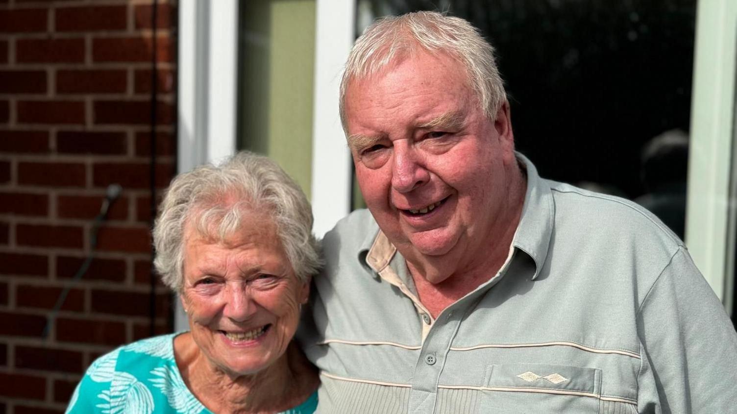 Michael Hamson and Judith Tomblin outside Mr Hamson's property. He has his arm around her and they are standing in front of some patio doors. 