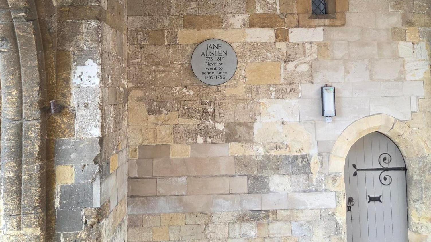 A grey plaque commemorating Jane Austen on a stone wall